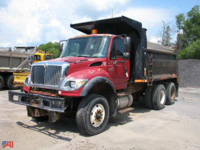 Dump truck showin g 2005 International 7600 WorkStar with red cab and black dump body in a yard.
