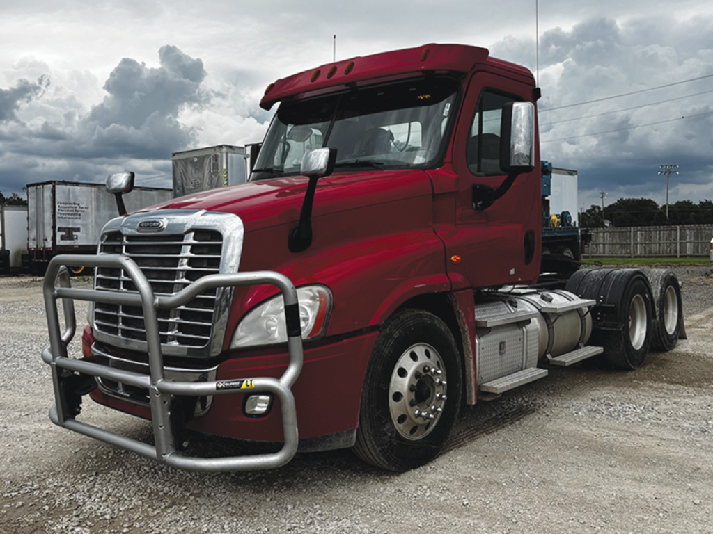 Freightliner Cascadia125 daycab truck in red, front grille with bumper guard, dual rear axles, exposed fuel tanks and side steps, cloudy sky.