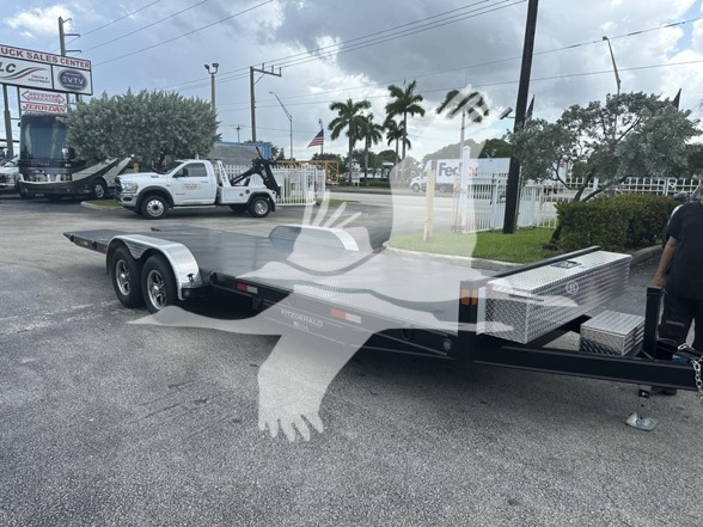 Flatbed trailer showing Dual-axle with long flat deck and metal diamond plate toolbox near front, hitch and stabilizer jack visible.