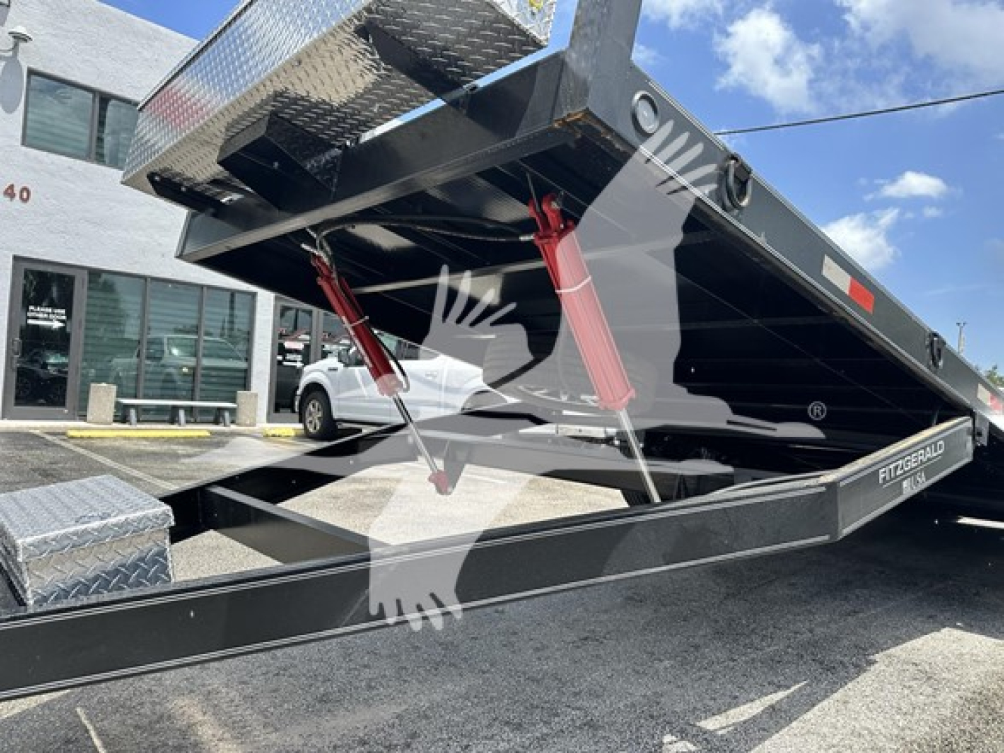 Unknown 24 ft trailer in lowered position with dual red hydraulic supports, black flatbed, and diamond plate toolbox/wheel area visible.