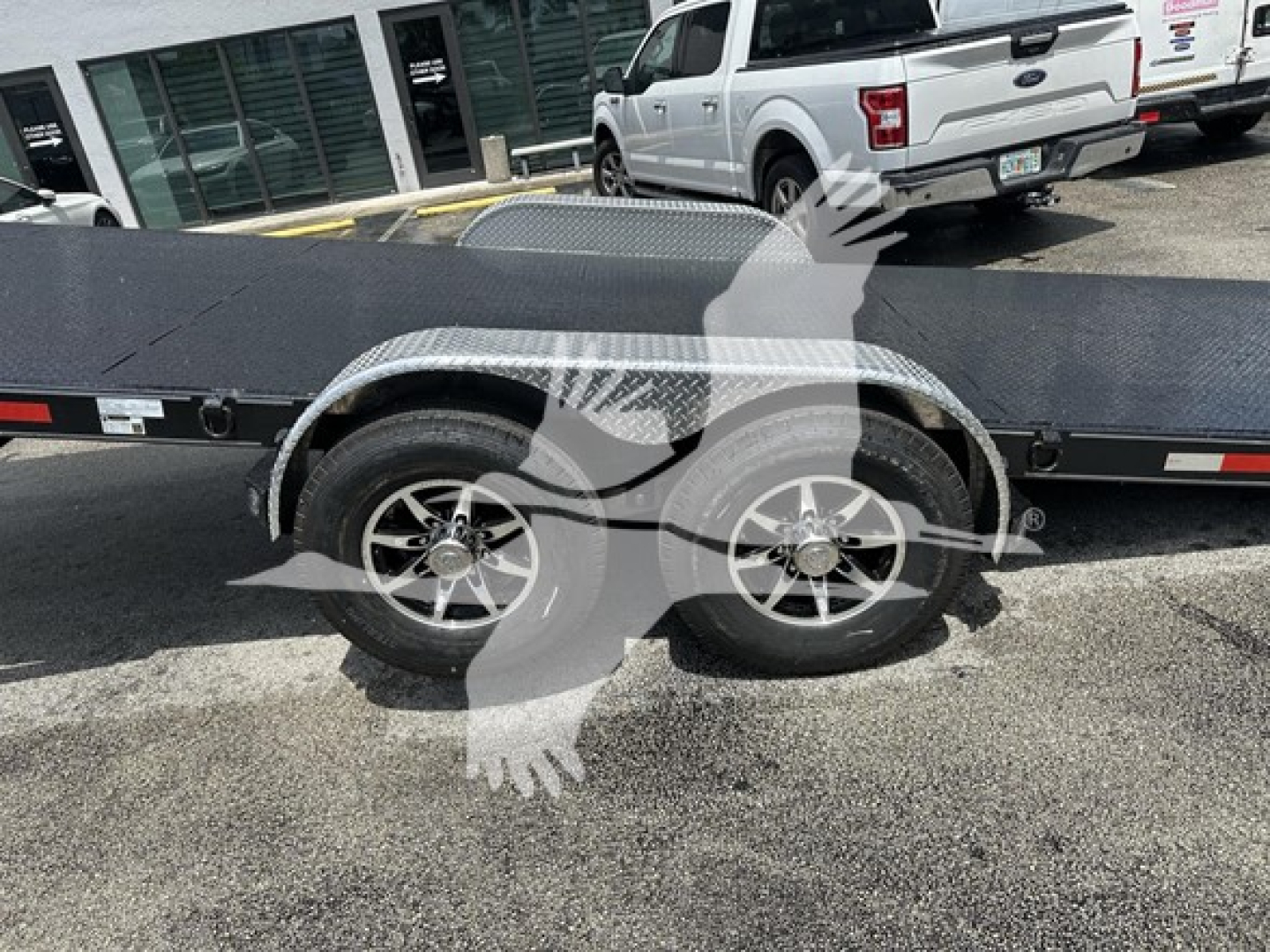 Dual-axle flatbed trailer with diamond plate fender and alloy wheels. Side profile shows two wheels and a portion of the trailer deck.