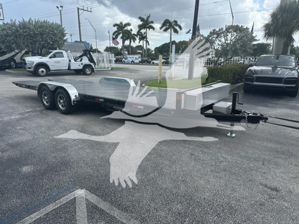Flatbed trailer with dual rear axles and gooseneck hitch in an outdoor lot, aluminum deck, 24 ft length, with nearby vehicles and palm trees.