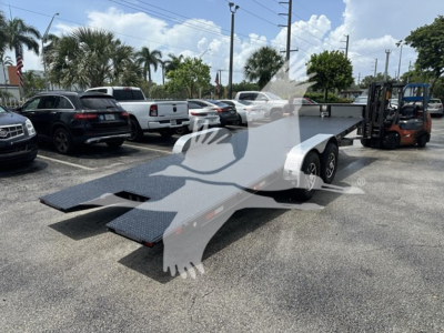 Trailer with dual-axle flatbed car hauler in outdoor lot, ramp/ loading ramps extended, forklift in background, palm trees and vehicles around.