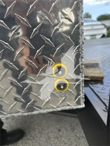 Diamond plate trailer edge with two yellow-labeled pushbuttons; arrows point in and out near control indicators on a metal surface.
