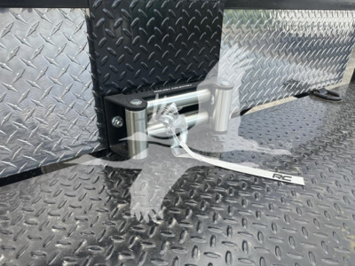 Trailer hitch or tow accessory on diamond plate trailer surface, showing a concealed stake with steel bolts and a silver hitch pin at the edge of a textured metal floor.