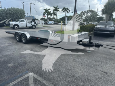 Flatbed trailer with dual rear axles and gooseneck hitch in an outdoor lot, aluminum deck, 24 ft length, with nearby vehicles and palm trees.