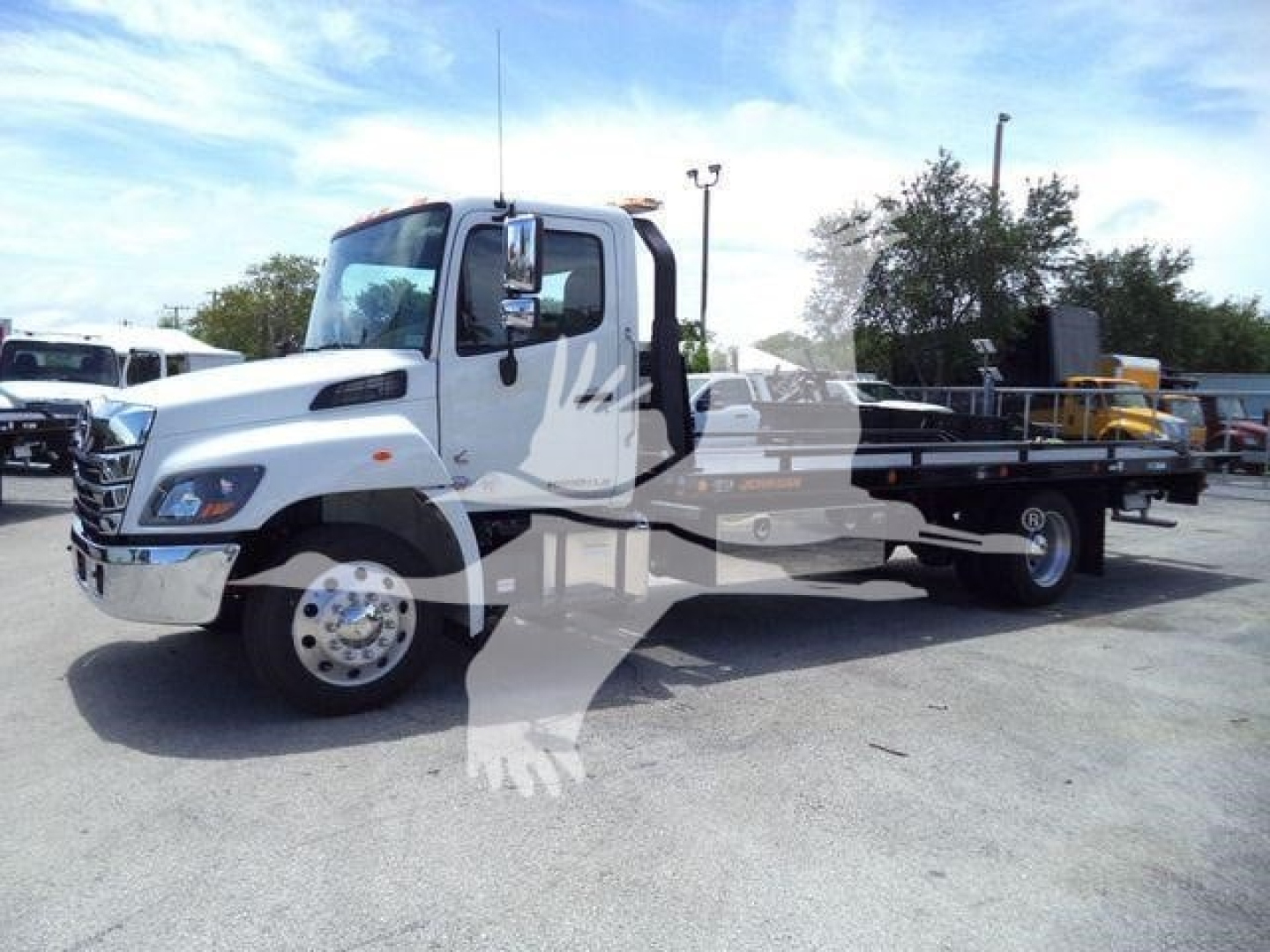 Truck viewed from side showing a white 2026 Hino L6 rollback hauler with extended chassis and dual rear wheels.