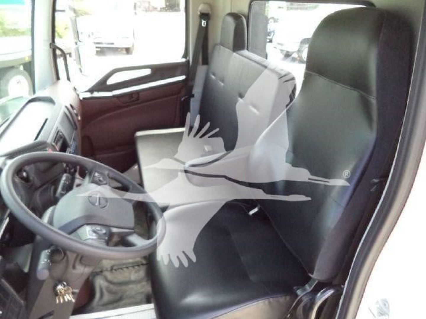 Truck cab interior showing driver's seat and front bench with black vinyl seats, steering wheel, and dashboard in a Hino L6 cab.