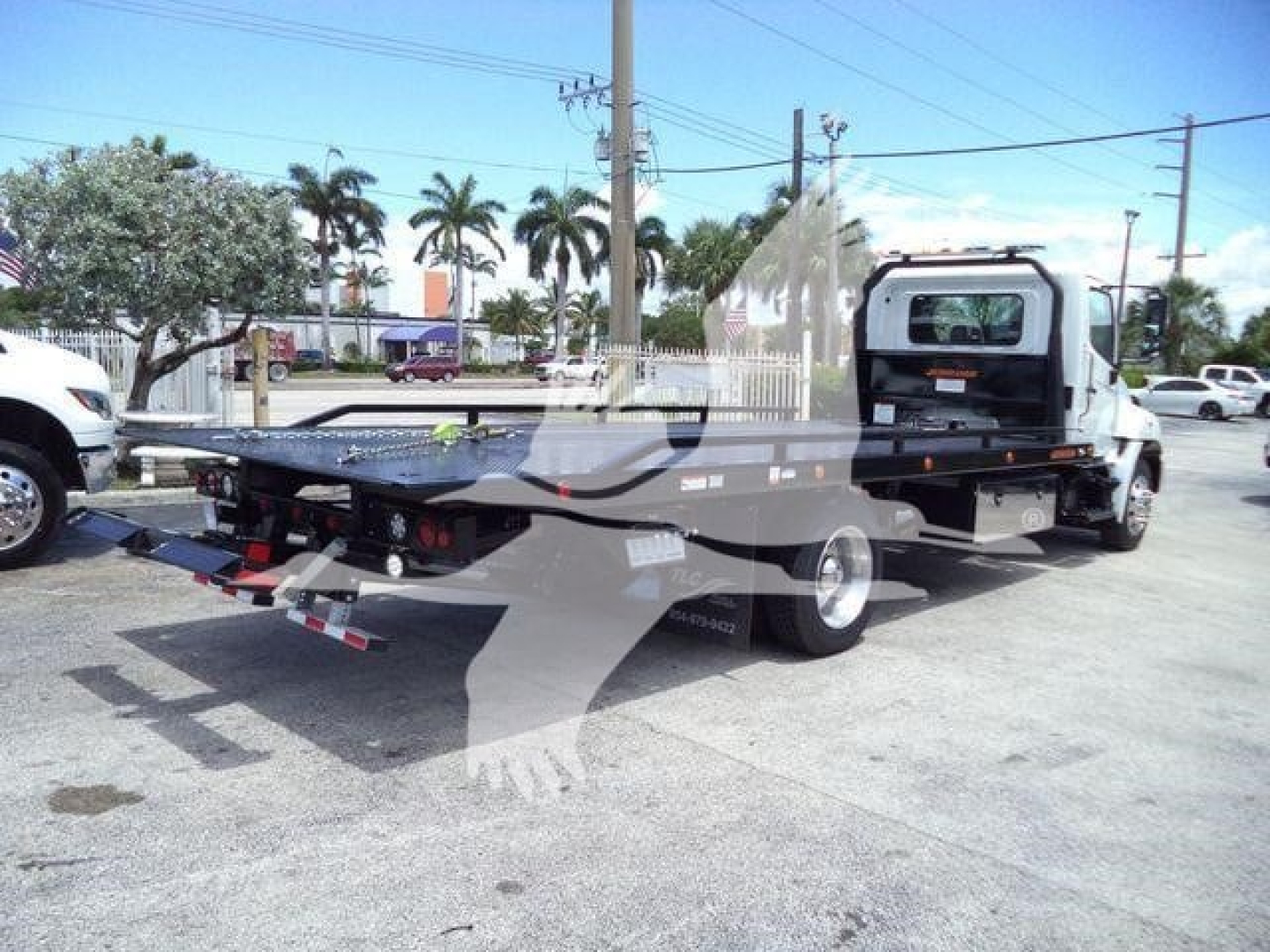 Flatbed tow truck in view showing rollback equipment and bed ramps.