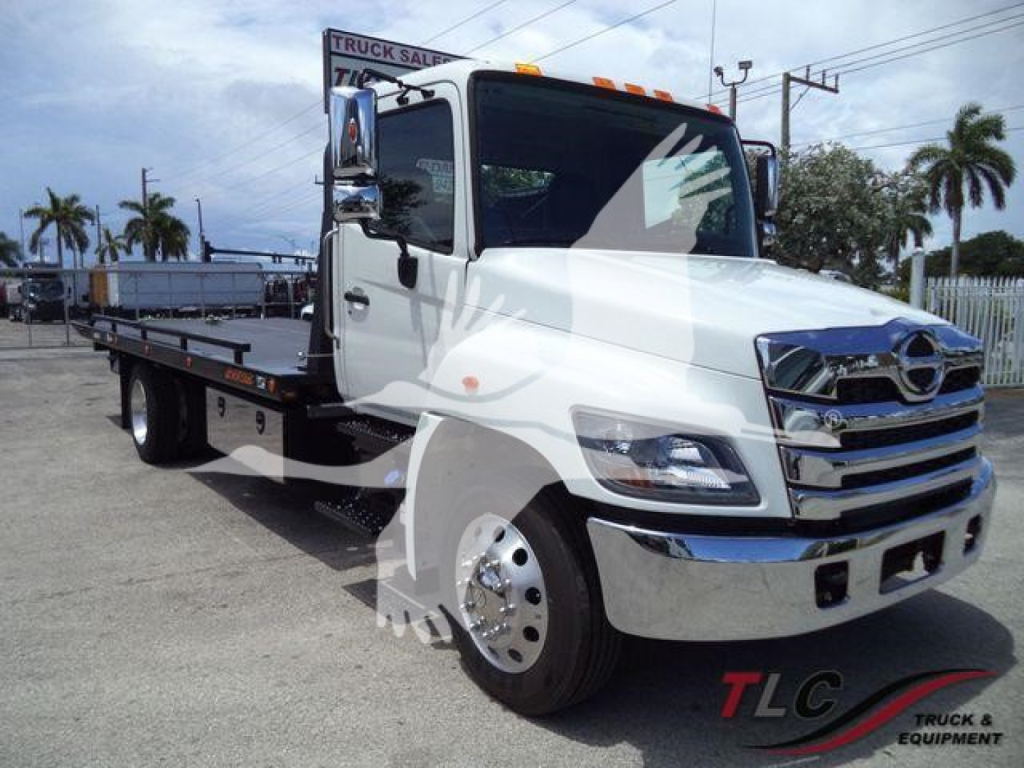Flatbed tow truck front-left view with white cab, chrome grille, and black bed. Visible text includes TLC Truck & Equipment watermark. No other legible labels or numbers.