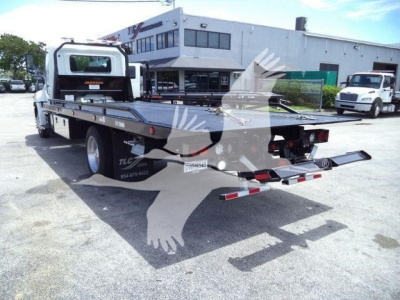 Flatbed tow truck rear view showing rollout bed and hydraulic controls with Hino branding and dealership background