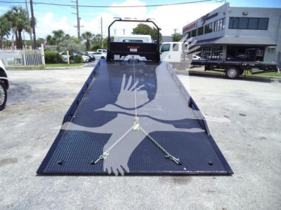 Truck rollback flatbed loader showing expanded metal surface with two tied-down chains and hooks, front cab visible in distance.