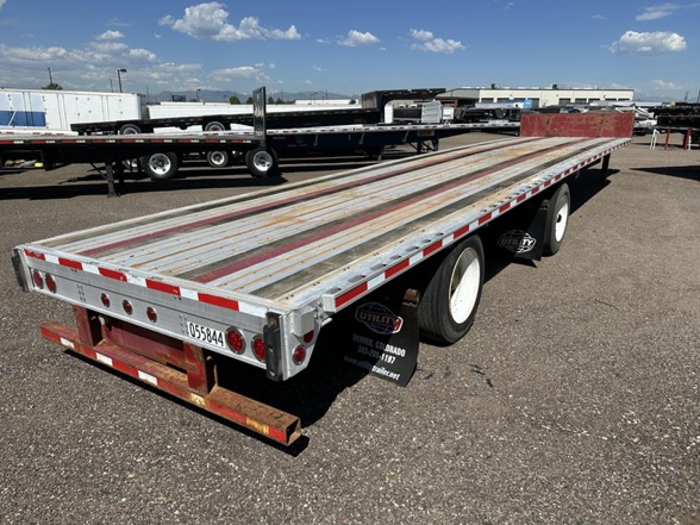 Flatbed trailer with long aluminum deck, dual rear axles, and wooden planks; Fontaine spread air combo drop deck trailer in a used lot.