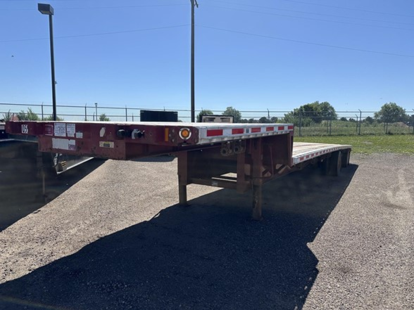 Flatbed trailer showing drop deck with red frame and long deck, undercarriage visible, used condition.