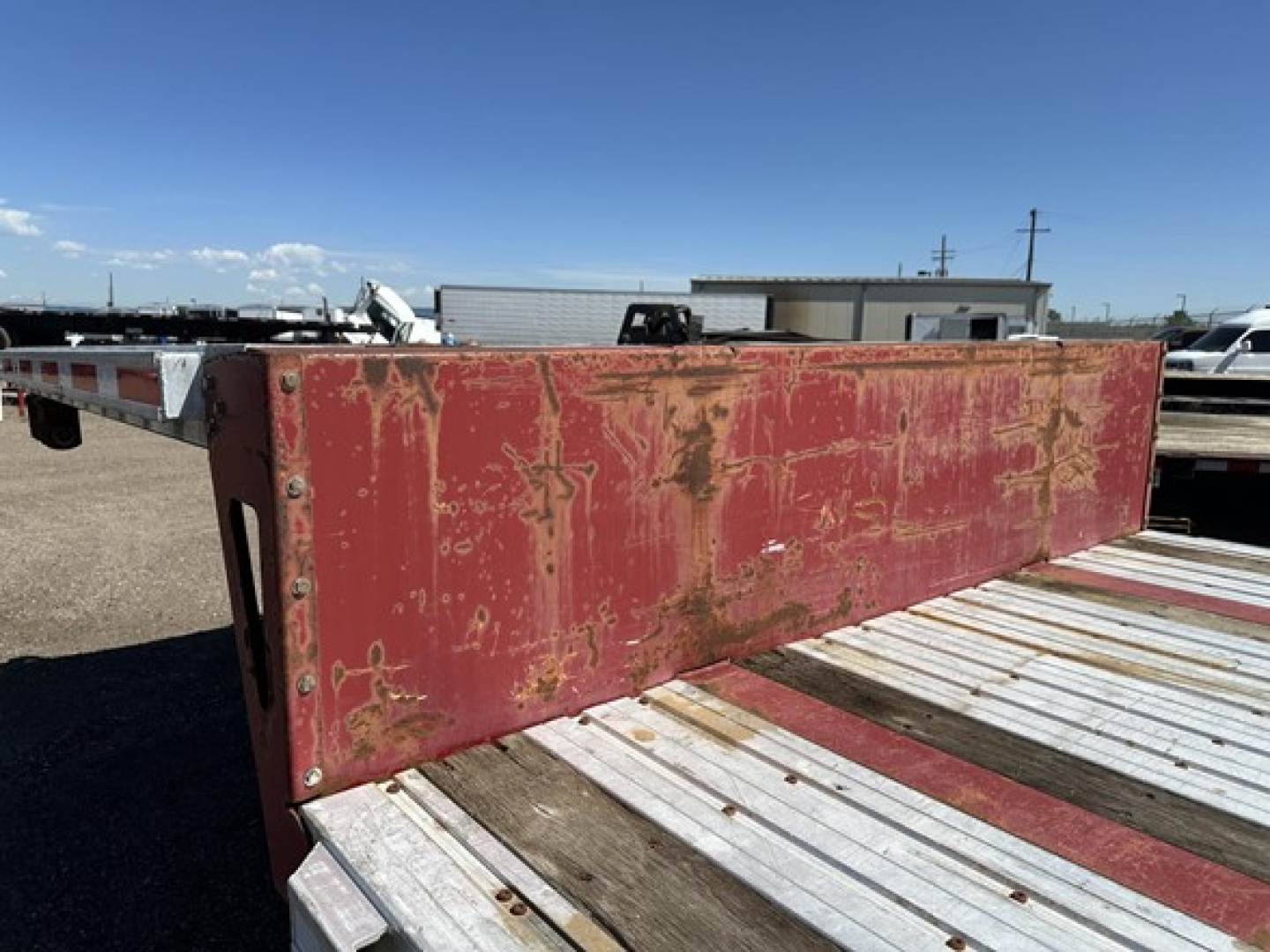 Truck trailer deck showing red drop deck side with worn paint and exposed metal, Fontaine spread-air combo drop deck trailer in field