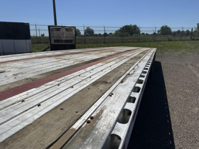 Flatbed trailer deck showing weathered wood planks with metal edge and stake pockets along the side.