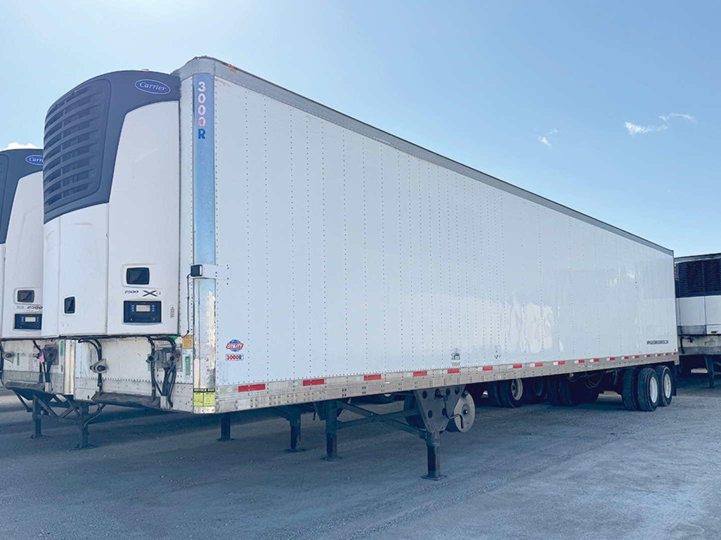 Utility reefer trailer in a yard showing Thermo King unit at the front and a white 53-foot refrigerated box with blue vertical stripe near the door.