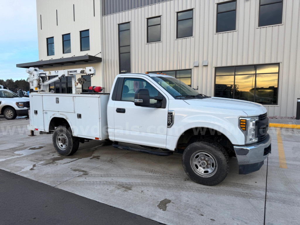 White 2019 Ford F-250 Super Duty XL service truck with utility bed and bucket lift, side view showing pallet and building in background.