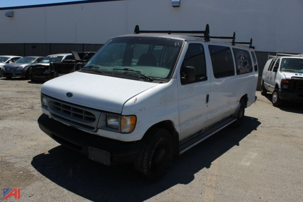 Ford E350 full-size van in front view showing roof rack and black front bumper, white body, daylight.