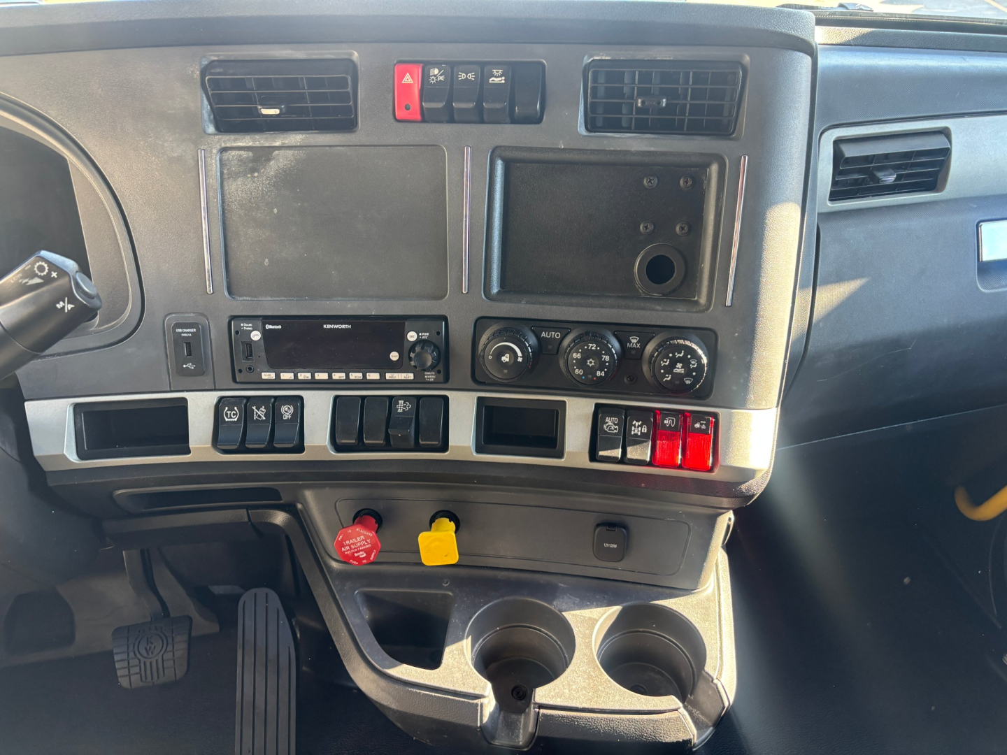 Dash and center console of a Kenworth truck cab showing climate controls, storage compartments, cup holders, and control switches.