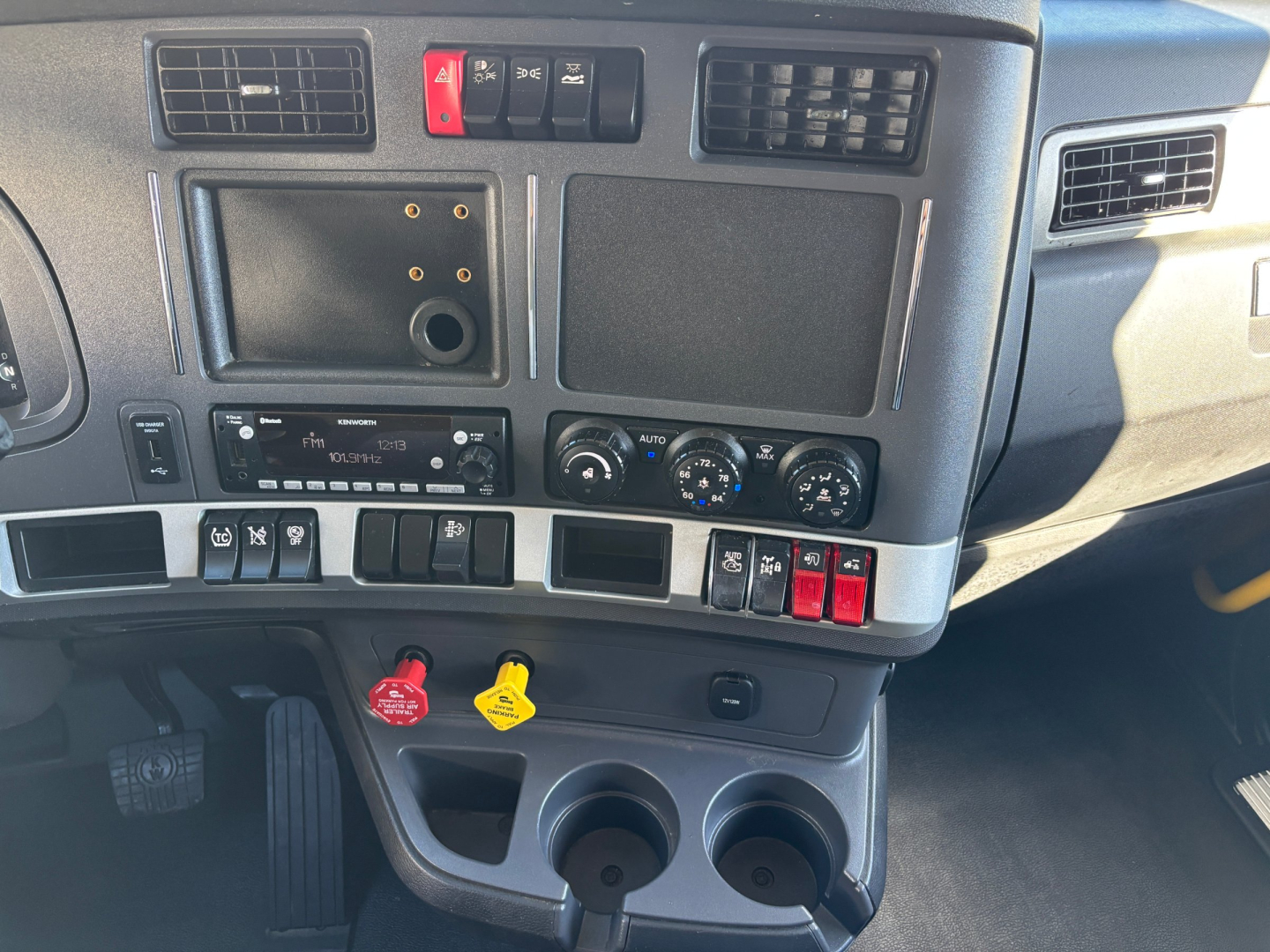 Kenworth T680 dash and center console showing controls, switches, and two cup holders with red and yellow caps.