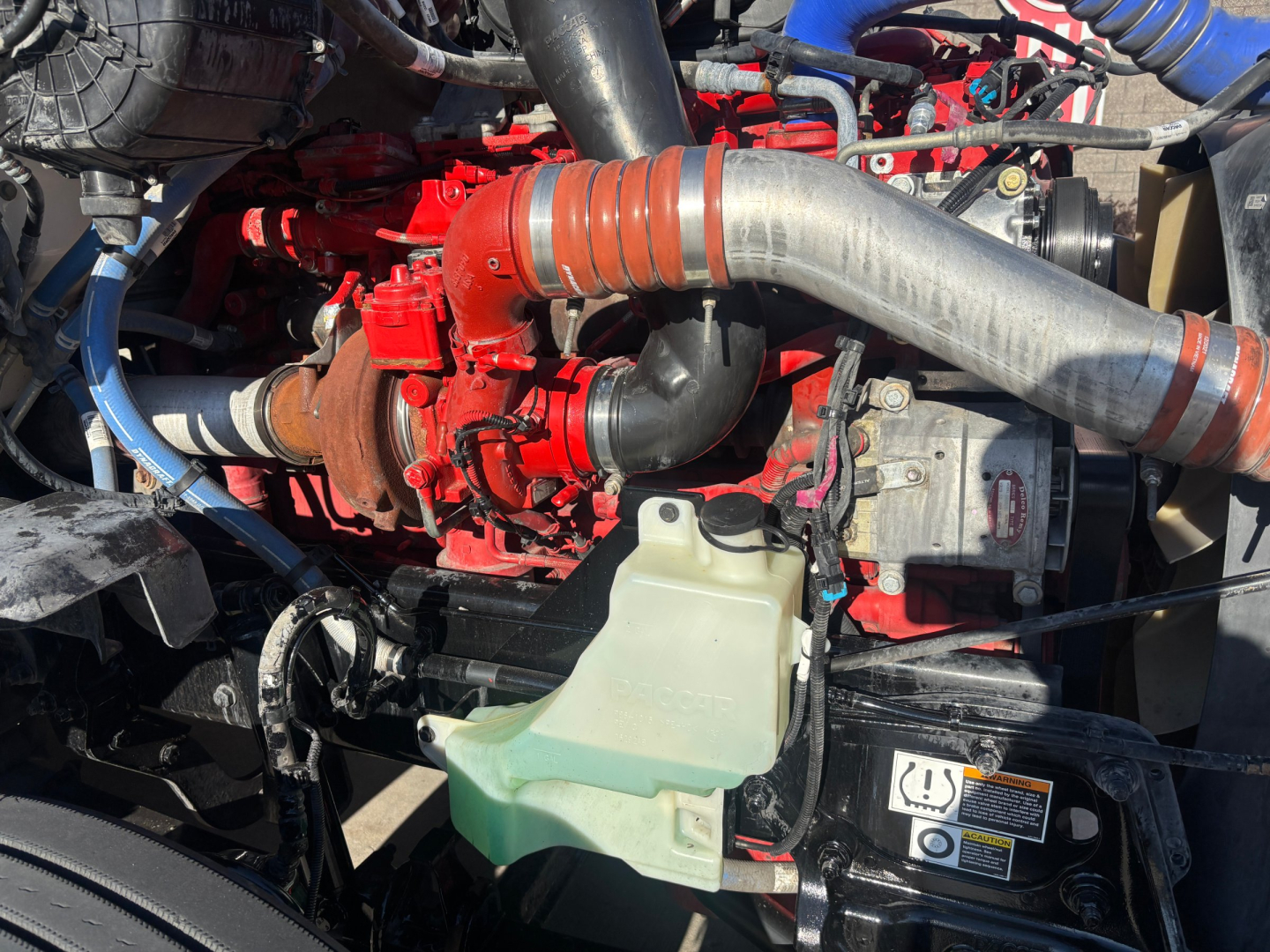 Kenworth T680 engine bay with red turbocharger, large gray intake pipe, green coolant reservoir, and various hoses.