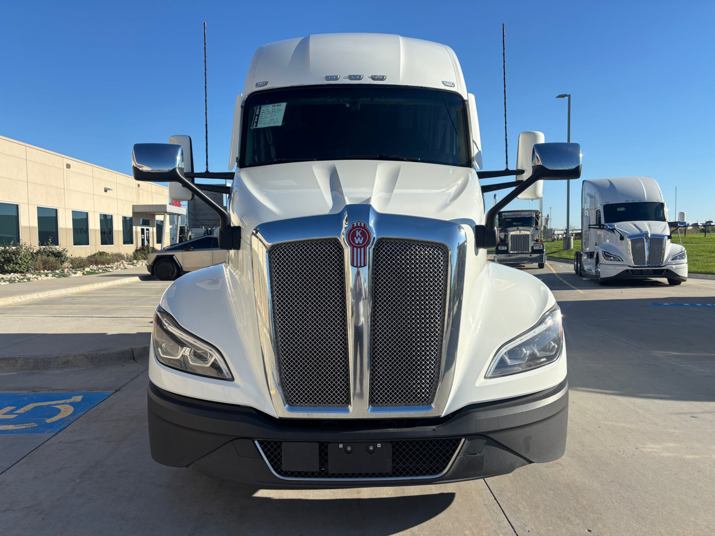 Front view of a white Kenworth truck cab with large grille and emblem, headlights, and side mirrors; no visible text legible on components.