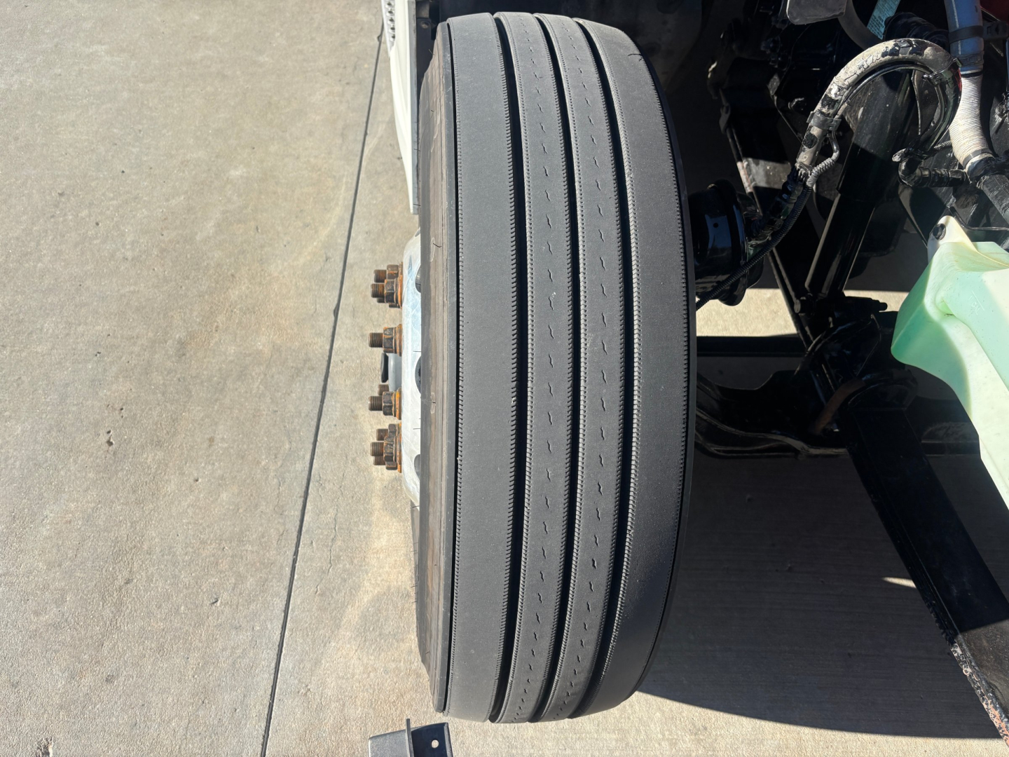 Kenworth T680 front wheel and axle area showing dual-tire design, rim studs, and suspension components.