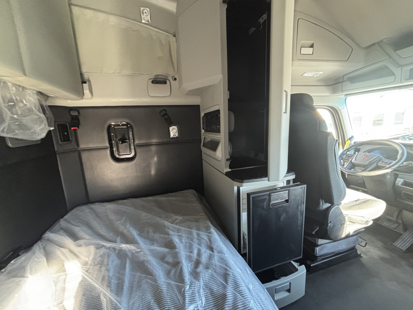 Kenworth T680 sleeper cab interior showing driver seat and bunk area with overhead storage and control panels.