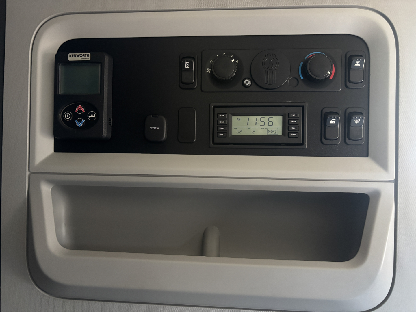 Kenworth T680 cab interior control panel showing HVAC knobs, a digital monitor, and a Kenworth auxiliary device panel