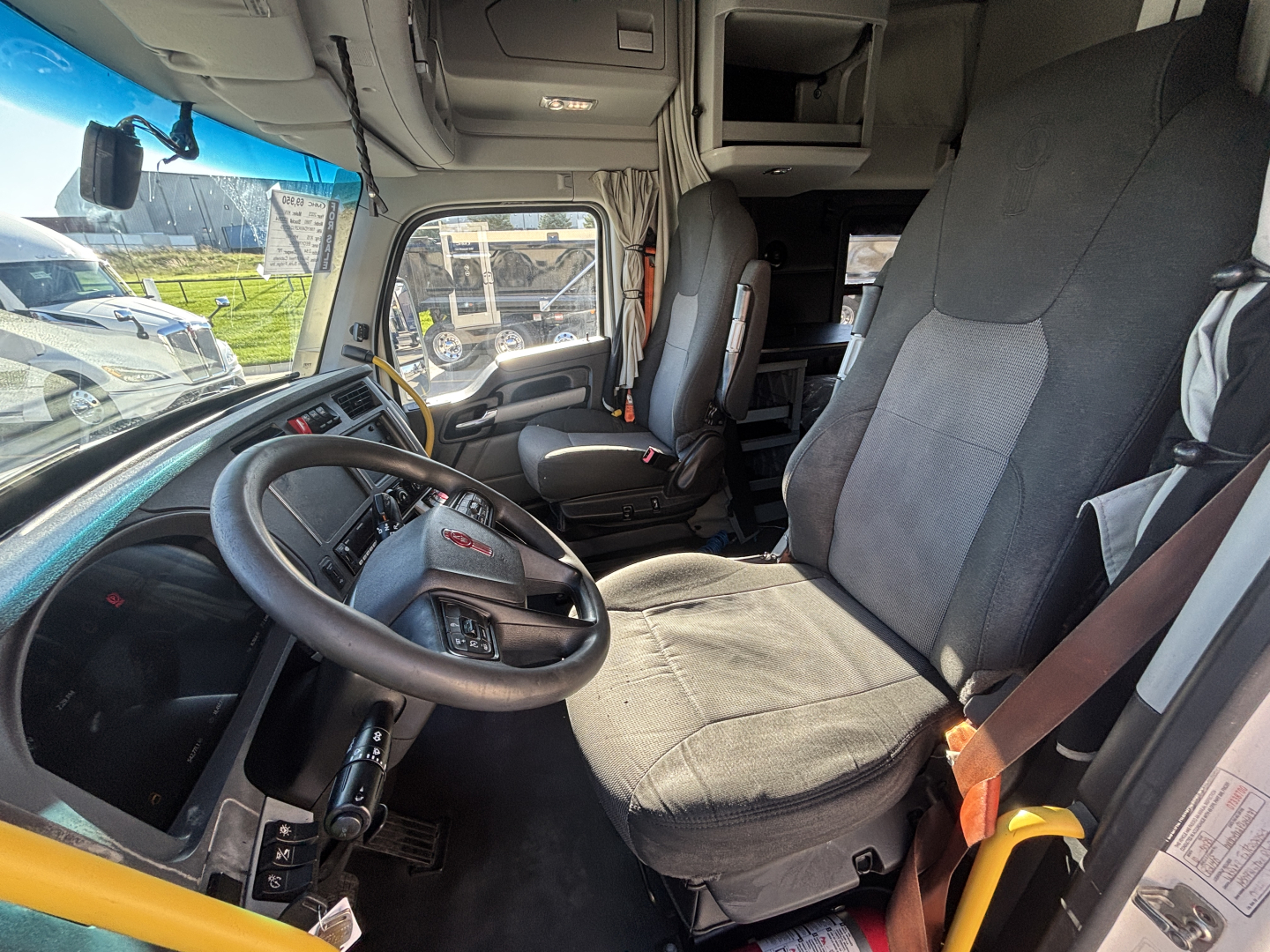 Kenworth T680 truck interior cab view showing driver seat and dashboard with steering wheel and passenger seat.