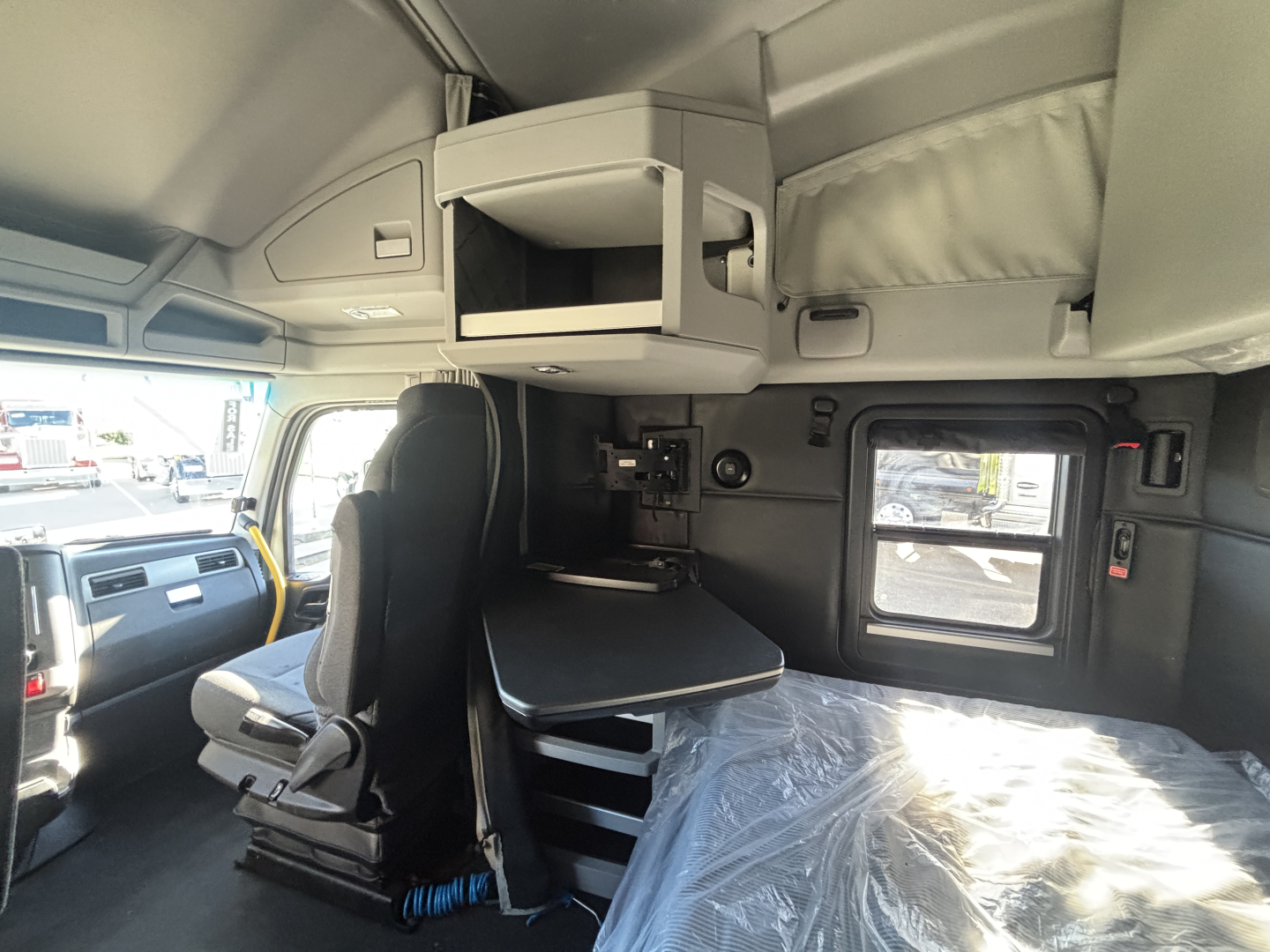 Interior of a Kenworth T680 cab showing sleeper area, overhead storage, fold-out table, and side windows.