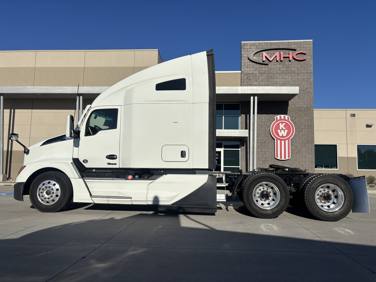 2023 Kenworth T680 side view showing tractor cab and dual rear axles in front of a dealership building.
