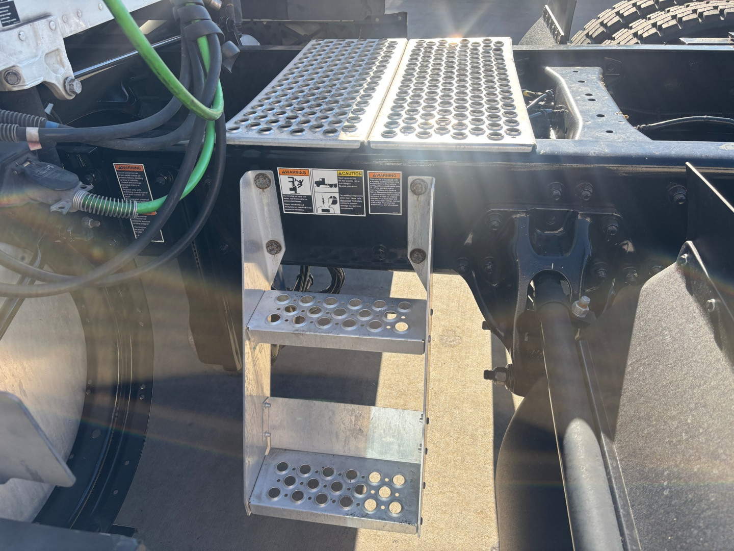 Kenworth T680 truck engine bay step with perforated metal steps and cab access area showing battery box and wiring.