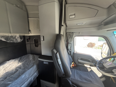 Truck cab interior of a 2023 Kenworth T680 showing driver seat, sleeper bed, and dashboard in-service 1XKYD49X2PJ242179