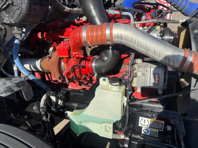 Kenworth T680 engine bay with red turbocharger, large gray intake pipe, green coolant reservoir, and various hoses.