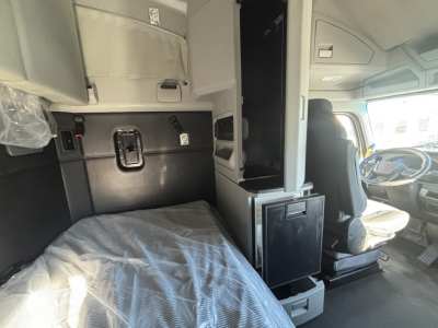 Kenworth T680 sleeper cab interior showing driver seat and bunk area with overhead storage and control panels.
