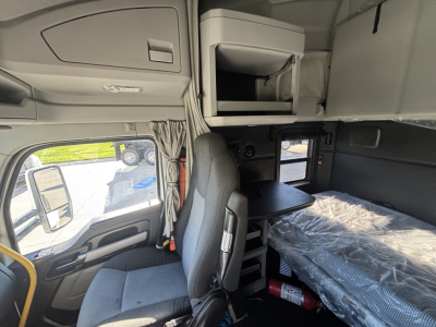 Kenworth T680 truck cab interior showing sleeper area with overhead storage, table, and passenger seat; plastic-wrapped bed and window view.