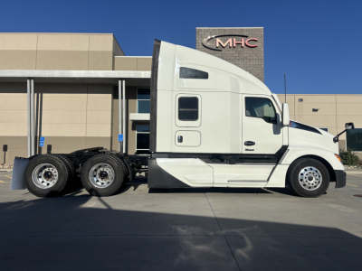 Kenworth T680 tractor-trailer in-service side profile showing white cab and dual rear axles with empty fifth wheel and MHC dealership building in background.