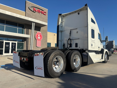 Kenworth T680 tractor with sleeper cab in a dealership lot, rear view showing 6 wheels and chassis, white cab and front mirrors visible.