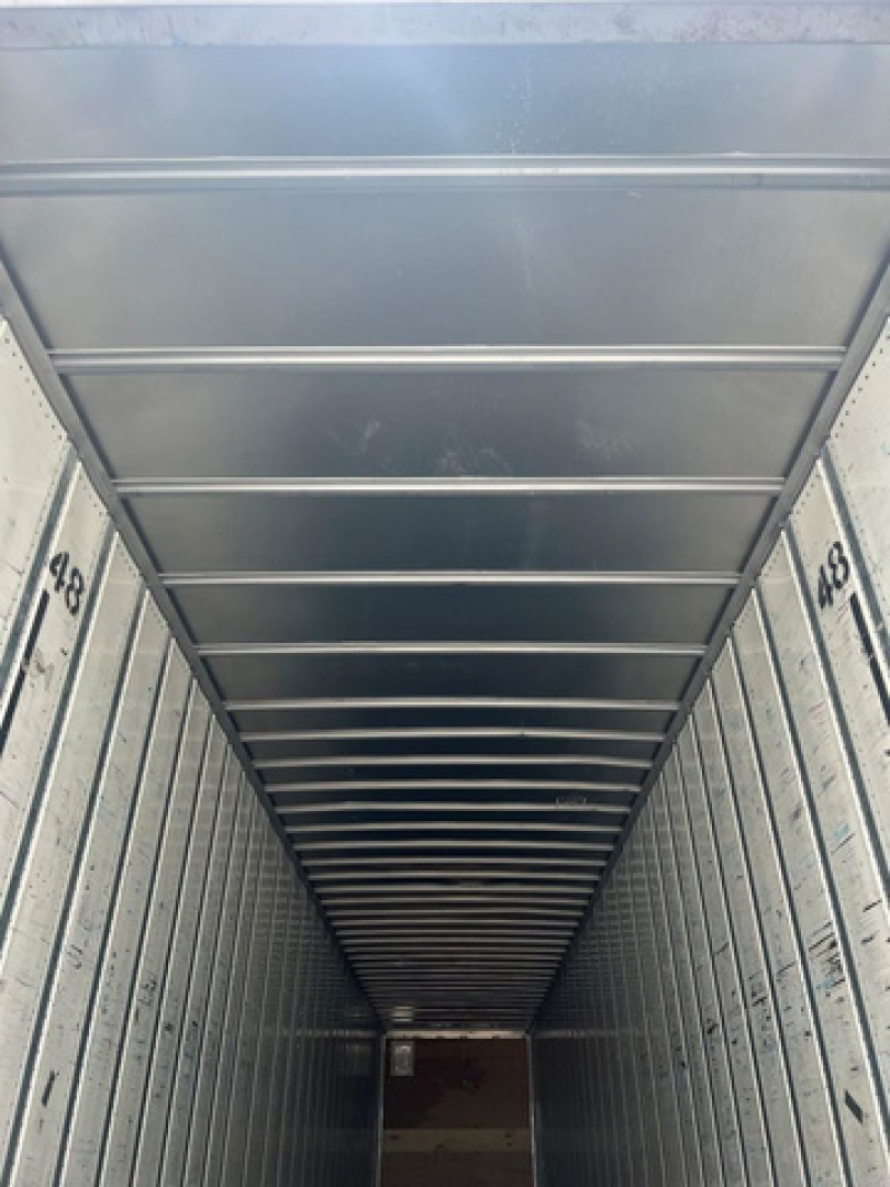 Interior of a cargo trailer showing metal sidewalls with overhead ribbing and numbered markings along the base, long narrow perspective toward the far end.