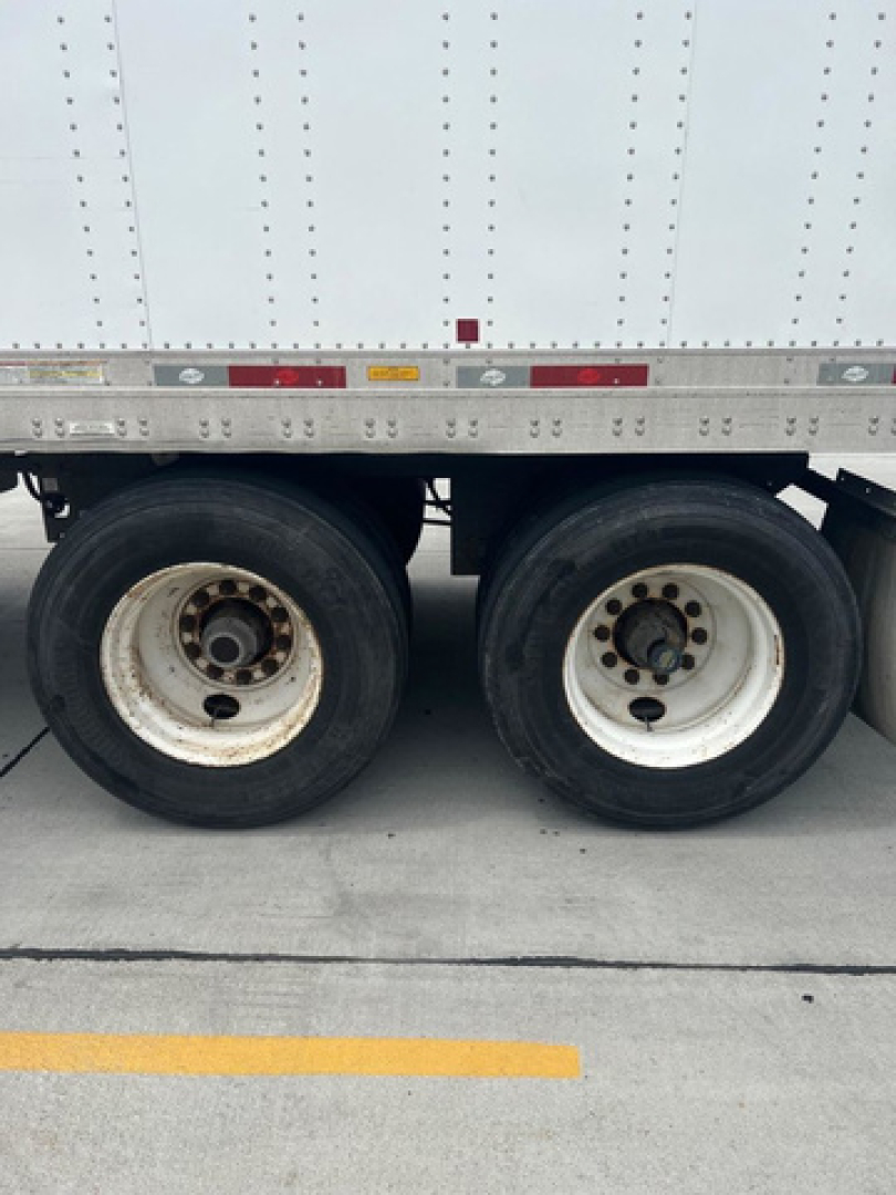 Dual rear trailer wheels and undercarriage of a white utility van trailer showing wheel rims and tandem axle.