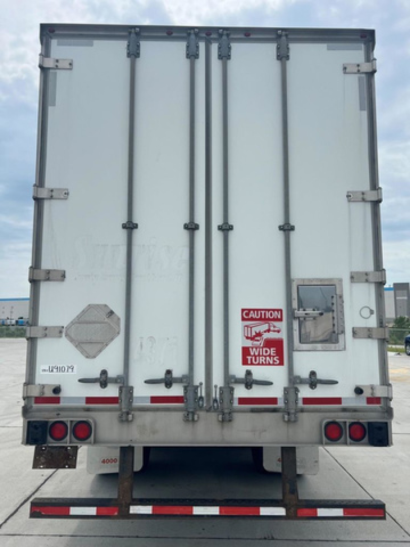 Rear view of a white box trailer with double rear doors, latches, and safety decals visible.