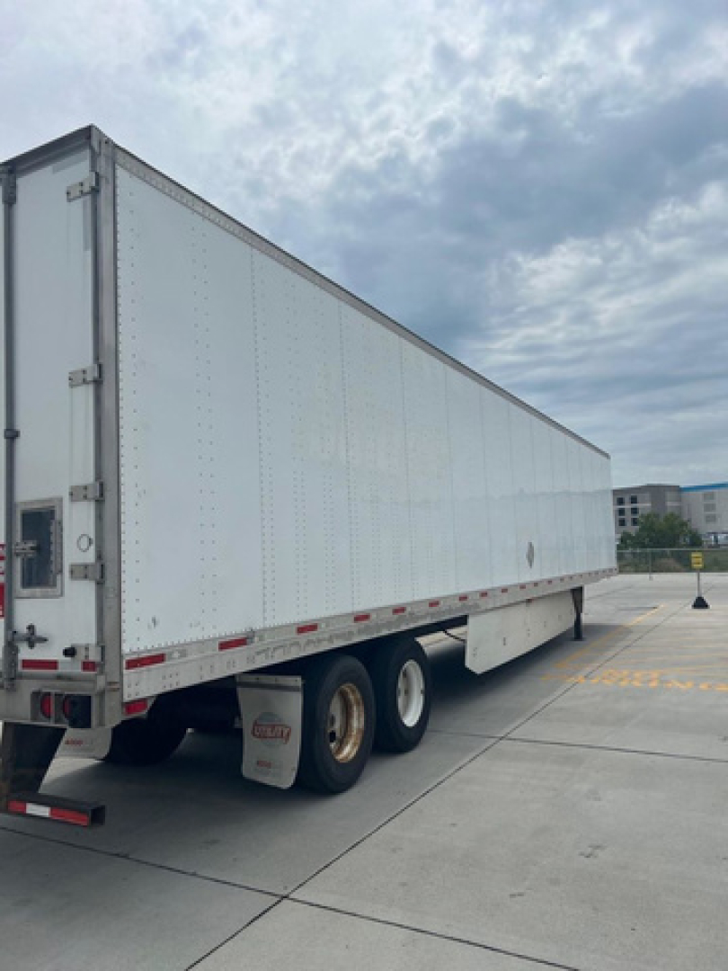 Utility van trailer showing side view of a white dry van trailer with dual rear wheels and red reflectors.
