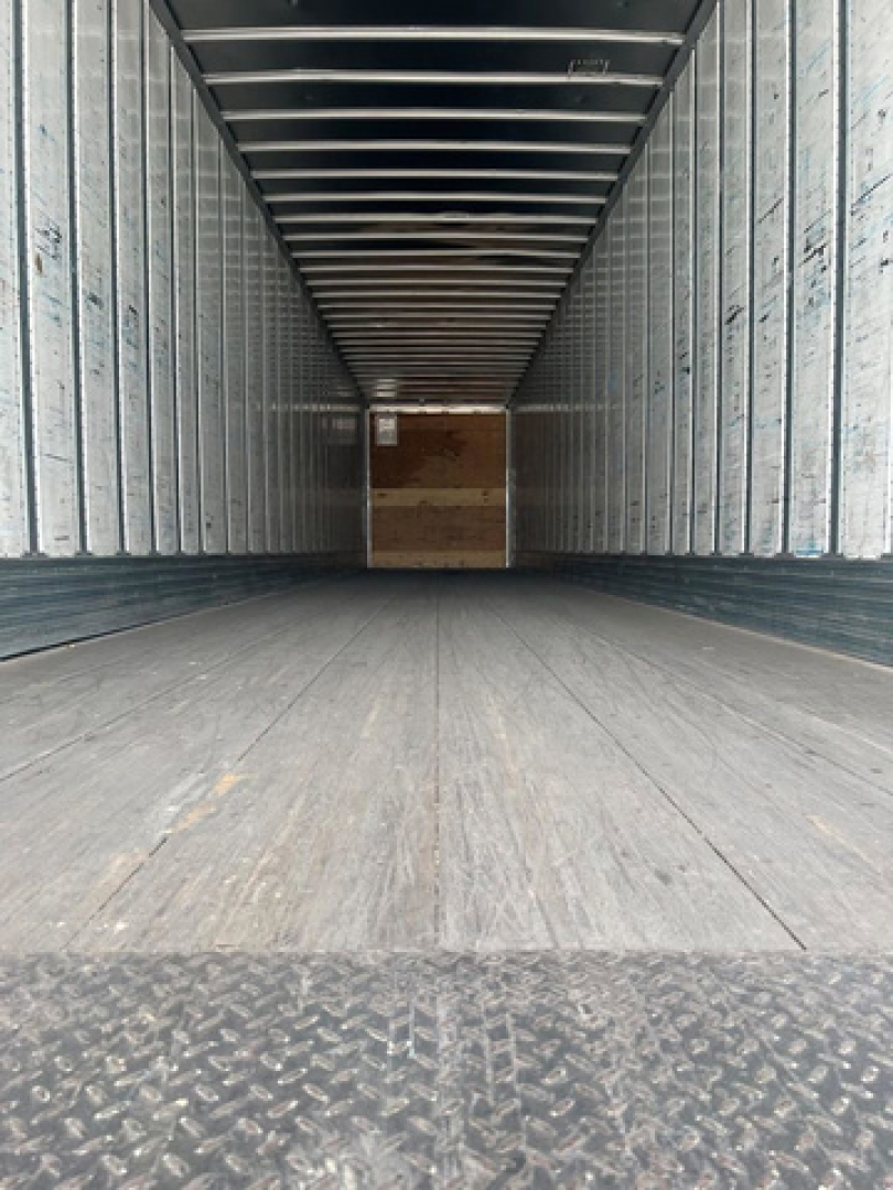 Trailer interior showing empty steel-sided cargo area with wooden bulkhead at far end and diamond plate entry threshold.