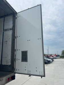 Open rear doors of a utility van trailer showing interior and the exterior door with a small vent/grille on the door pane; no legible model text visible in image.