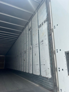 Interior of a trailer with metal walls and sliding door track; visible stamped numbers 481 and 53 102 on the side panel.