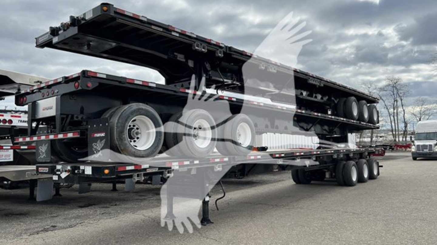 Manac extendable flatbed trailer with dual rear axles and sixth wheel set, showcasing side rails and deck undercarriage. Some stickers visible on rear and side.