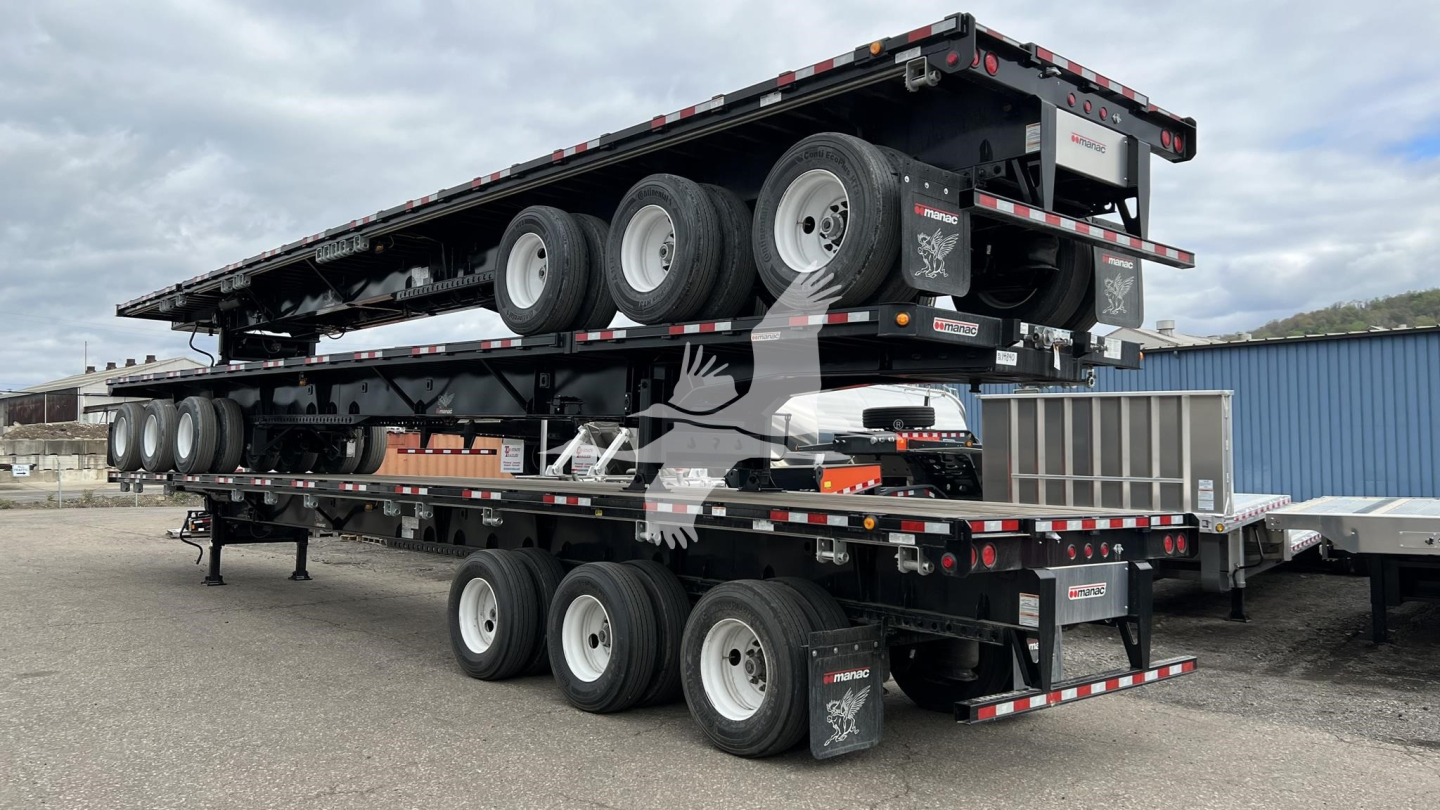 Manac extendable flatbed trailer showing multiple axles and a lowered center deck with reflectors and branding, side ramps, and rear extension components.