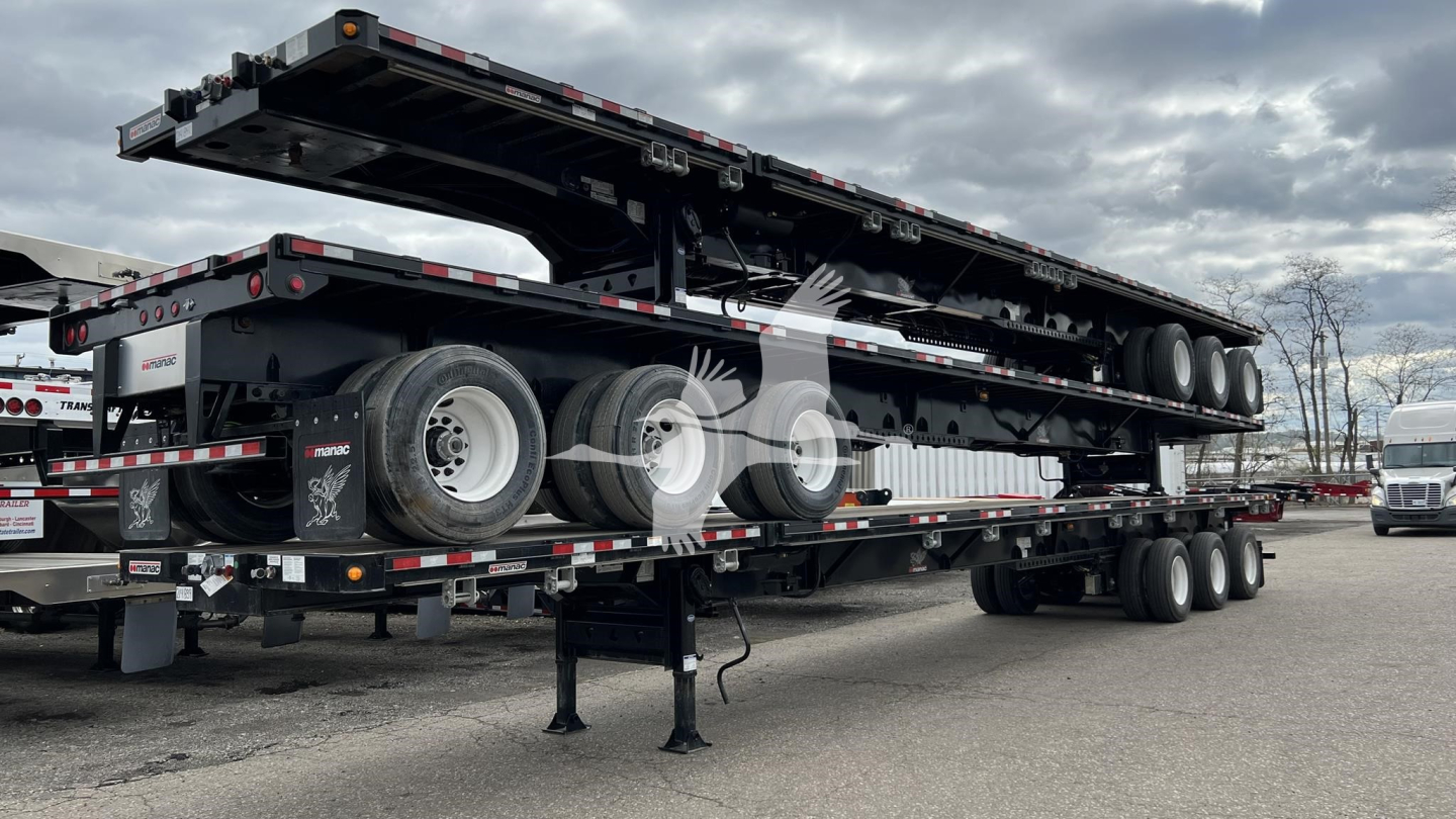 Flatbed trailer with extendable section raised, Manac brand extendable flatbed trailer, triple-axle with stacked wheels, safety reflectors, and support legs visible.